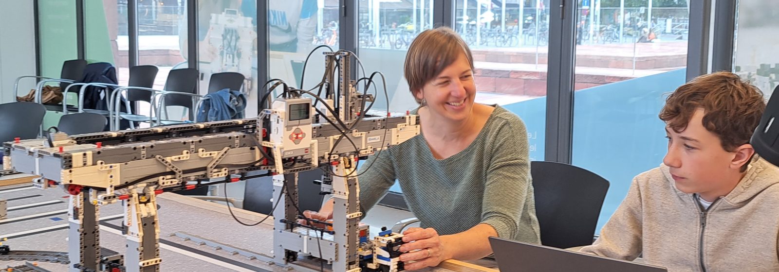 Leerkracht programmeert robots samen met een leerling.